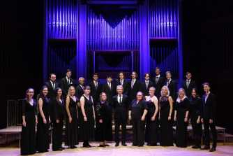 The 24 standing on stage in a group in concert dress